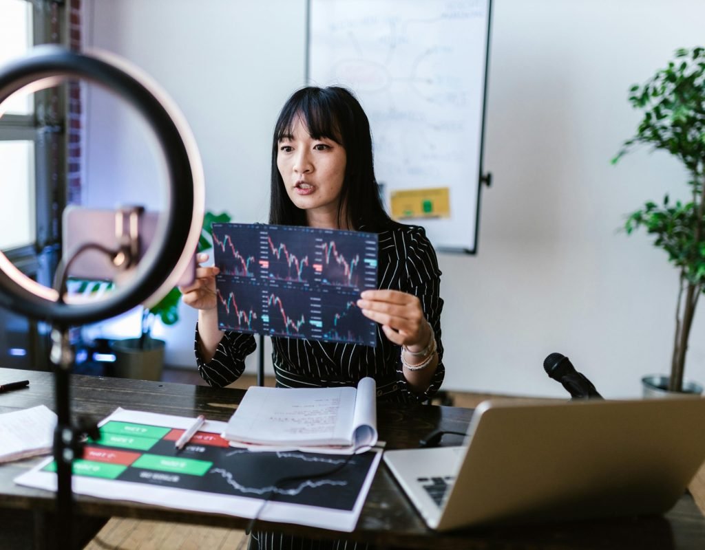 A woman vlogger discusses stock market trends using charts in a home studio.